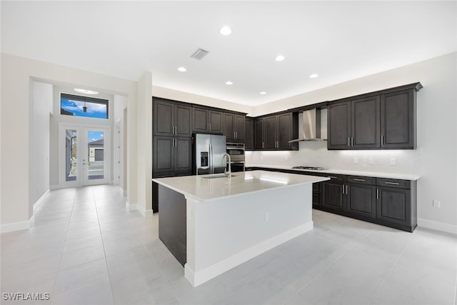 kitchen with a center island with sink, sink, wall chimney exhaust hood, french doors, and stainless steel appliances