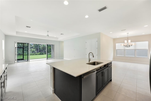 kitchen featuring an island with sink, a tray ceiling, sink, decorative light fixtures, and stainless steel dishwasher