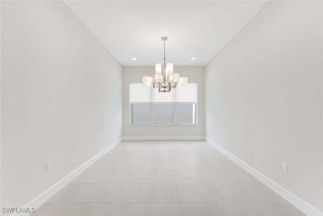 tiled spare room featuring an inviting chandelier