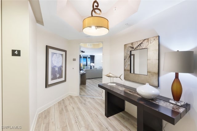 hall with a tray ceiling and light wood-type flooring