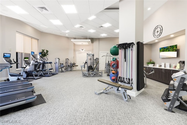 exercise room with a paneled ceiling, a towering ceiling, and light colored carpet