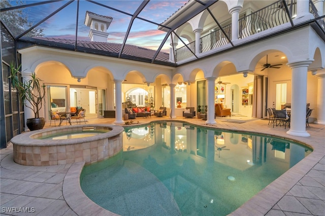 pool at dusk with an in ground hot tub, ceiling fan, a patio, and a lanai