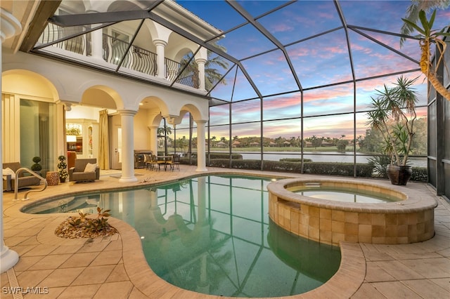 pool at dusk featuring a water view, an in ground hot tub, glass enclosure, and a patio area