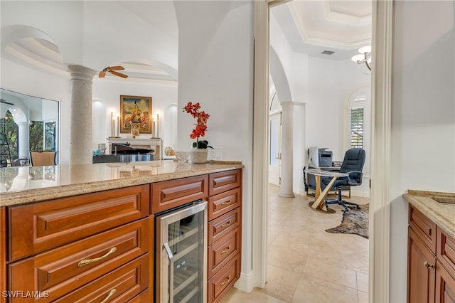 kitchen with ornate columns, wine cooler, crown molding, a raised ceiling, and light stone counters