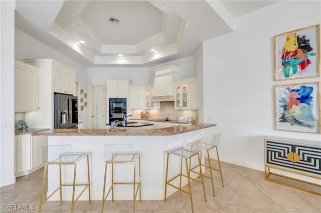 kitchen with light stone countertops, black appliances, a tray ceiling, and a kitchen bar