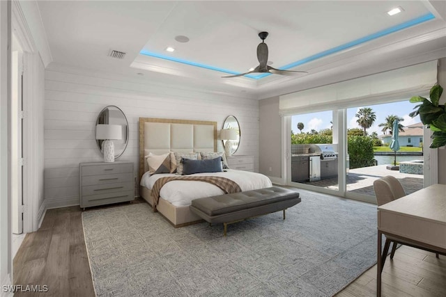 bedroom with light hardwood / wood-style flooring, ceiling fan, access to exterior, and a raised ceiling