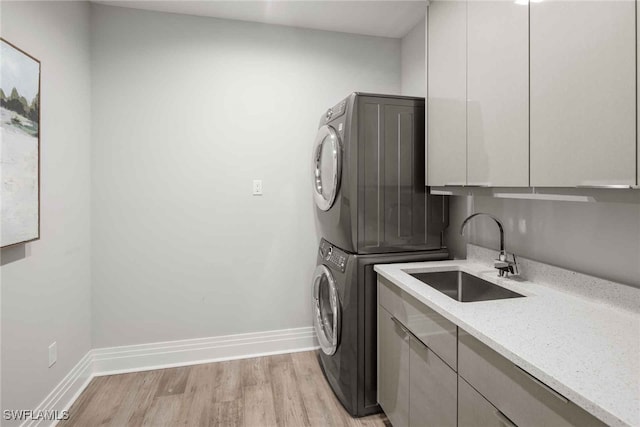 clothes washing area with cabinets, stacked washer / dryer, sink, and light wood-type flooring