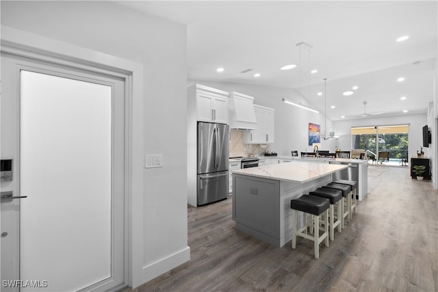 kitchen with lofted ceiling, a kitchen island, stainless steel appliances, light stone countertops, and white cabinets