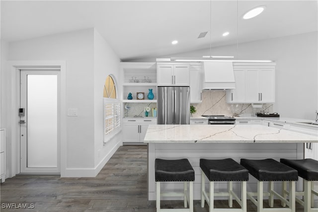 kitchen featuring stainless steel appliances, lofted ceiling, white cabinets, custom range hood, and a breakfast bar area