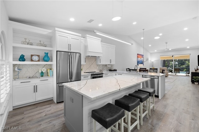 kitchen featuring appliances with stainless steel finishes, white cabinetry, kitchen peninsula, vaulted ceiling, and a breakfast bar area