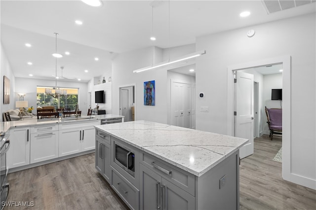 kitchen with stainless steel microwave, hanging light fixtures, sink, light stone counters, and a center island