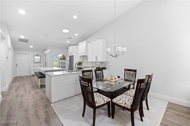 dining room with sink, an inviting chandelier, lofted ceiling, and light wood-type flooring