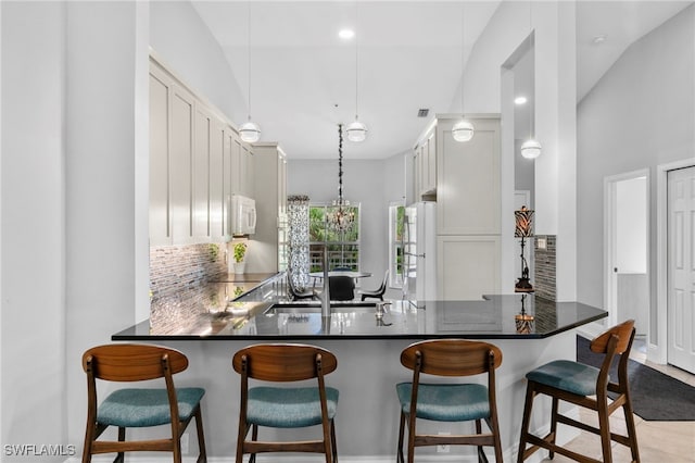 kitchen featuring kitchen peninsula, white cabinets, a breakfast bar, pendant lighting, and white appliances