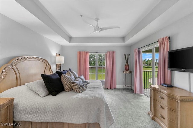 bedroom featuring multiple windows, access to exterior, a tray ceiling, and ceiling fan