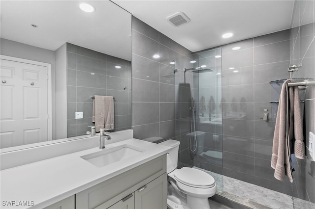 bathroom with tile walls, vanity, tiled shower, and toilet