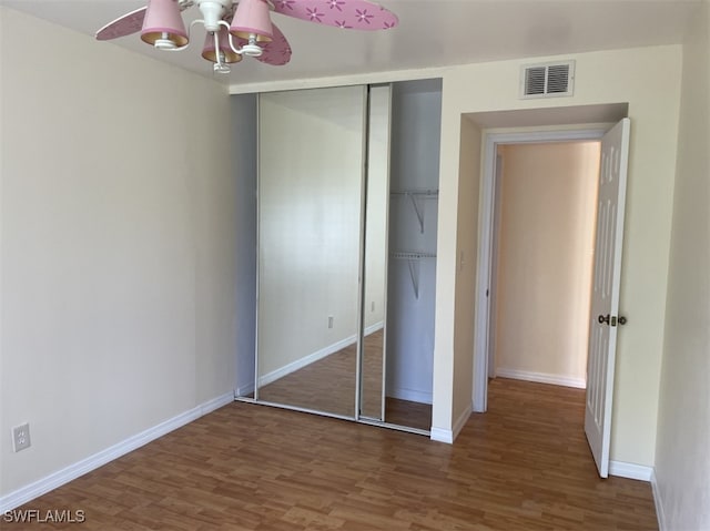 unfurnished bedroom with a closet, dark hardwood / wood-style flooring, and ceiling fan with notable chandelier