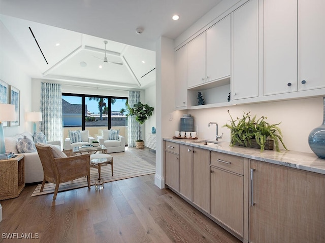 kitchen with sink, ceiling fan, light stone countertops, light brown cabinets, and light wood-type flooring