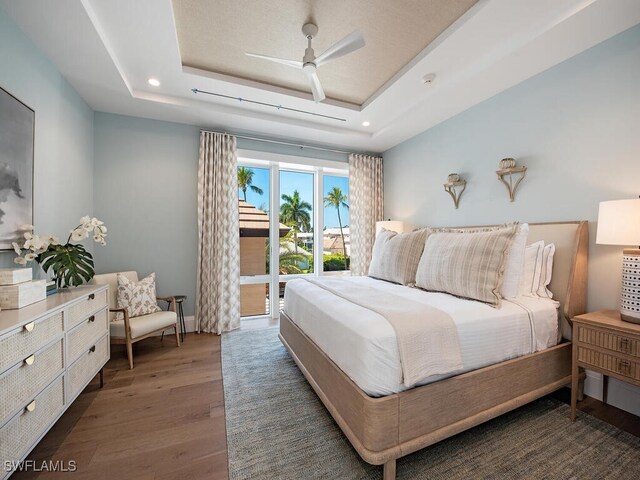 bedroom with access to exterior, a tray ceiling, dark hardwood / wood-style floors, and ceiling fan