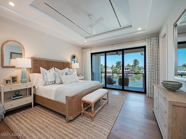 bedroom with access to exterior, light hardwood / wood-style floors, a raised ceiling, and ceiling fan