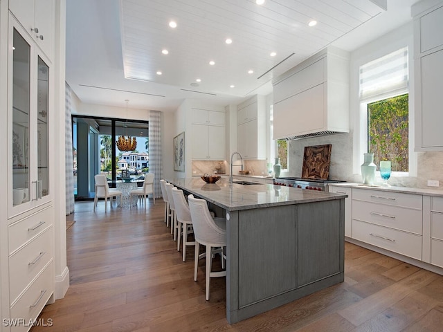 kitchen with premium range hood, a kitchen bar, sink, an island with sink, and white cabinets