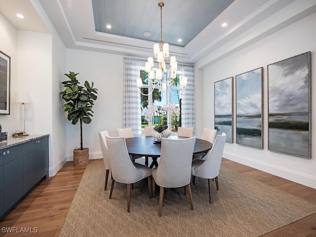 dining space with a notable chandelier, a tray ceiling, and dark wood-type flooring