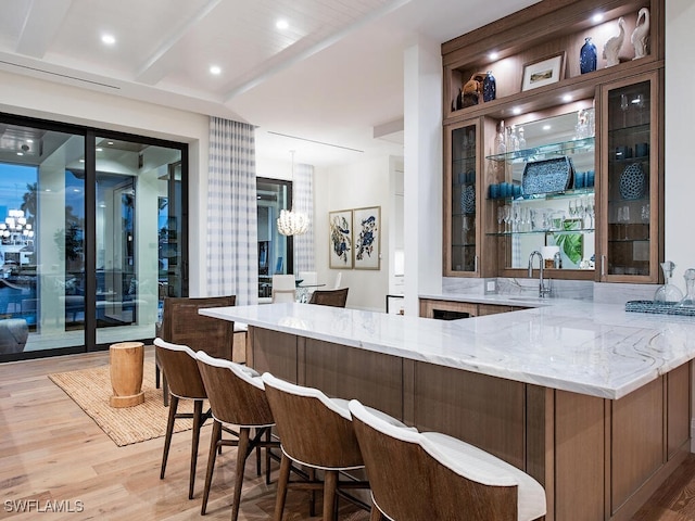 bar with light stone counters, sink, a chandelier, and light hardwood / wood-style floors