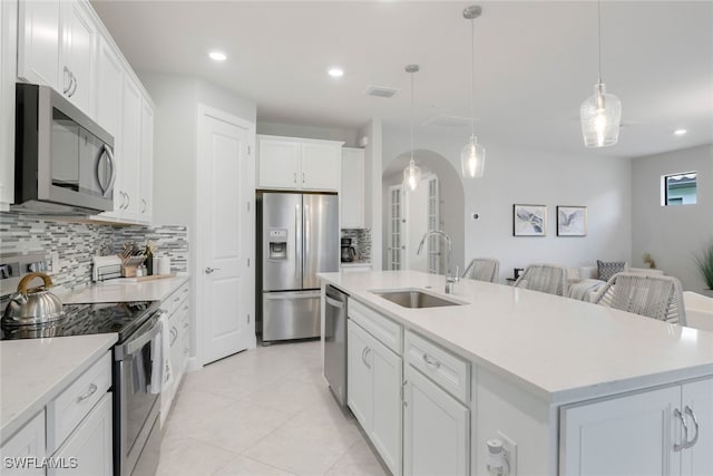 kitchen with sink, hanging light fixtures, an island with sink, white cabinetry, and stainless steel appliances