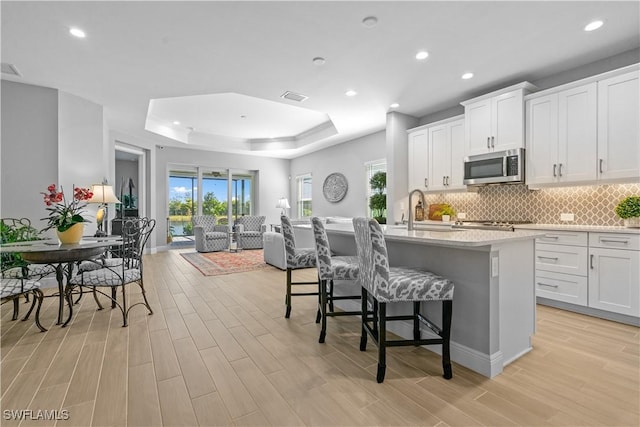 kitchen featuring white cabinetry, an island with sink, sink, a kitchen breakfast bar, and a raised ceiling