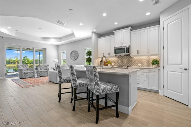 kitchen with white cabinets, sink, a tray ceiling, and a center island with sink