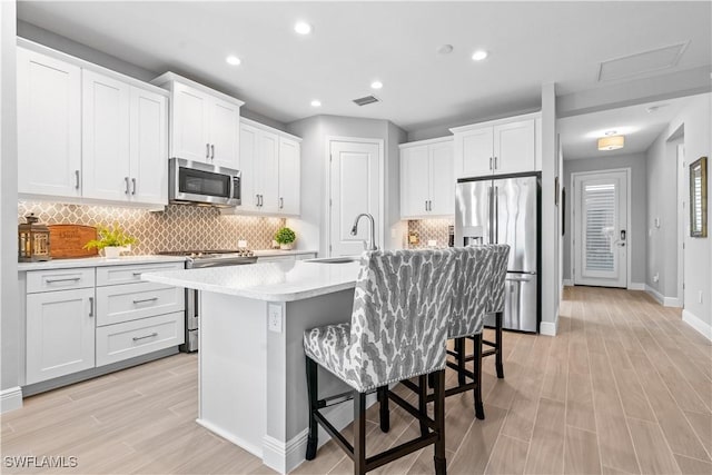 kitchen featuring a kitchen bar, an island with sink, appliances with stainless steel finishes, white cabinets, and sink