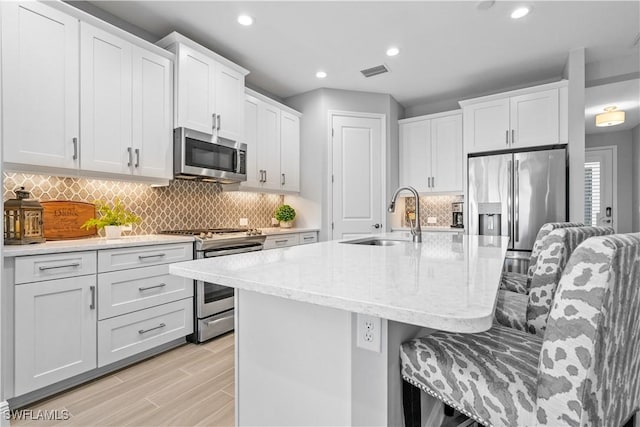 kitchen with a breakfast bar, sink, white cabinetry, a kitchen island with sink, and appliances with stainless steel finishes