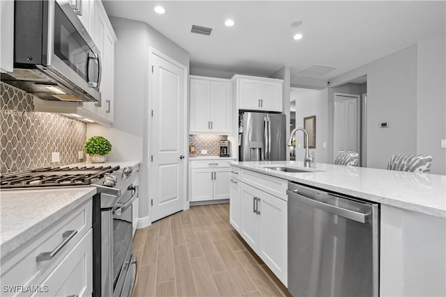 kitchen featuring stainless steel appliances, decorative backsplash, light stone countertops, white cabinets, and sink