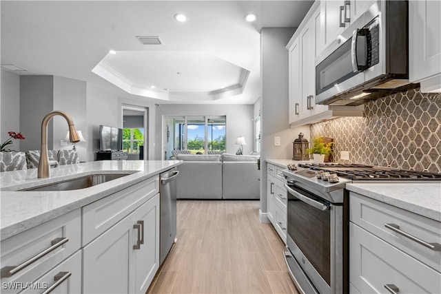 kitchen with a raised ceiling, sink, light wood-type flooring, stainless steel appliances, and white cabinets