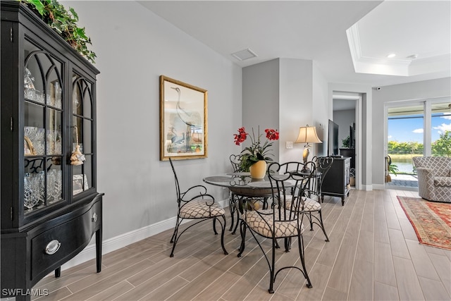 dining space with a tray ceiling, light hardwood / wood-style flooring, and ornamental molding