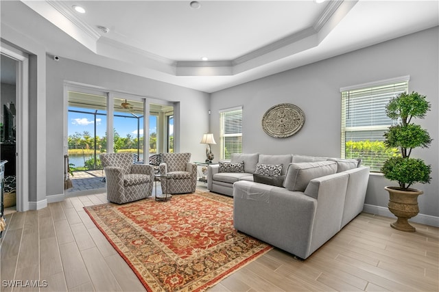 living room featuring a raised ceiling, a water view, and crown molding