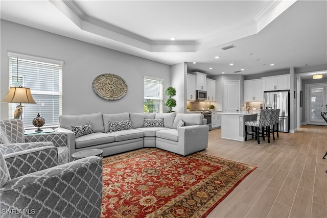 living room with crown molding, light wood-type flooring, and a tray ceiling