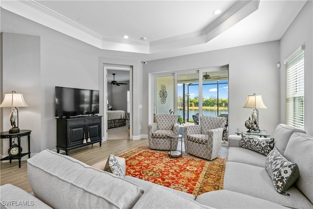 living room with light hardwood / wood-style floors, a tray ceiling, crown molding, and ceiling fan