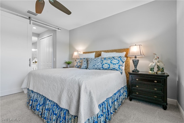 carpeted bedroom with ceiling fan, a closet, and a barn door