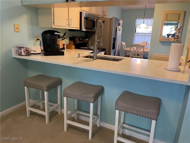 kitchen with white cabinets, hanging light fixtures, kitchen peninsula, stainless steel appliances, and light carpet