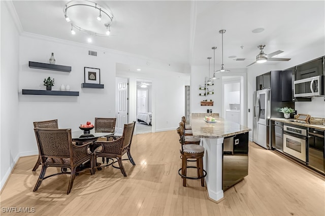 kitchen with light wood-type flooring, stainless steel appliances, decorative light fixtures, and light stone countertops