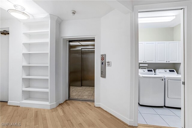 clothes washing area with washer and clothes dryer, light wood-type flooring, cabinets, and elevator