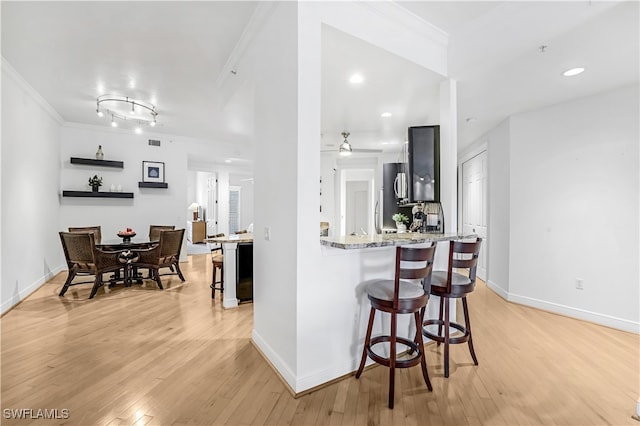 kitchen featuring kitchen peninsula, crown molding, light hardwood / wood-style floors, and a breakfast bar