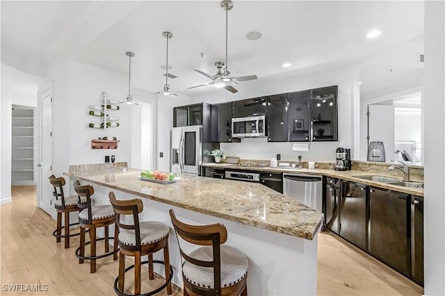 kitchen featuring kitchen peninsula, appliances with stainless steel finishes, decorative light fixtures, and light hardwood / wood-style flooring