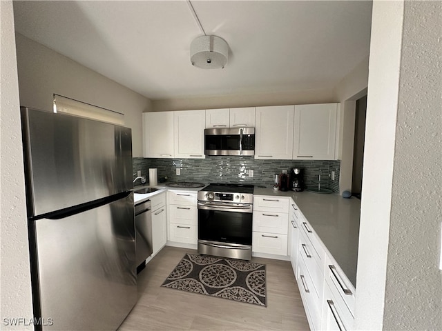 kitchen featuring decorative backsplash, sink, light wood-type flooring, white cabinetry, and appliances with stainless steel finishes