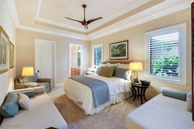 bedroom with connected bathroom, ornamental molding, light colored carpet, a raised ceiling, and ceiling fan