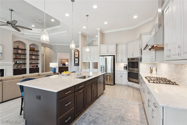 kitchen with pendant lighting, wall chimney exhaust hood, a large island with sink, and stainless steel appliances