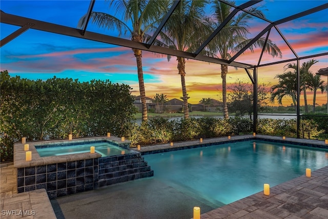 pool at dusk featuring glass enclosure and an in ground hot tub