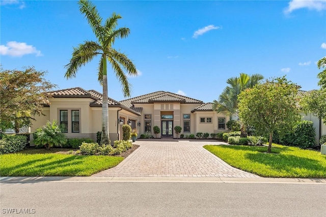 mediterranean / spanish-style home featuring a tile roof, stucco siding, an attached garage, french doors, and driveway