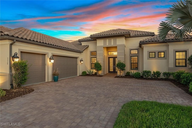 mediterranean / spanish-style house featuring a tile roof, stucco siding, an attached garage, french doors, and decorative driveway
