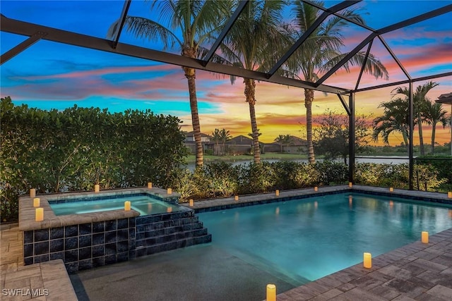 pool at dusk featuring glass enclosure, a pool with connected hot tub, and a patio area
